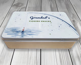 Personalised fishing snack tin with "Grandad's Fishing Snacks" lid, front view on wooden boards