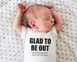 a baby laying on a bed wearing a shirt that says glad to be out i was running out of womb