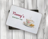 Personalised biscuit tin with the lid resting on the open tin on white wooden boards, watercolour rose teacup and biscuits design